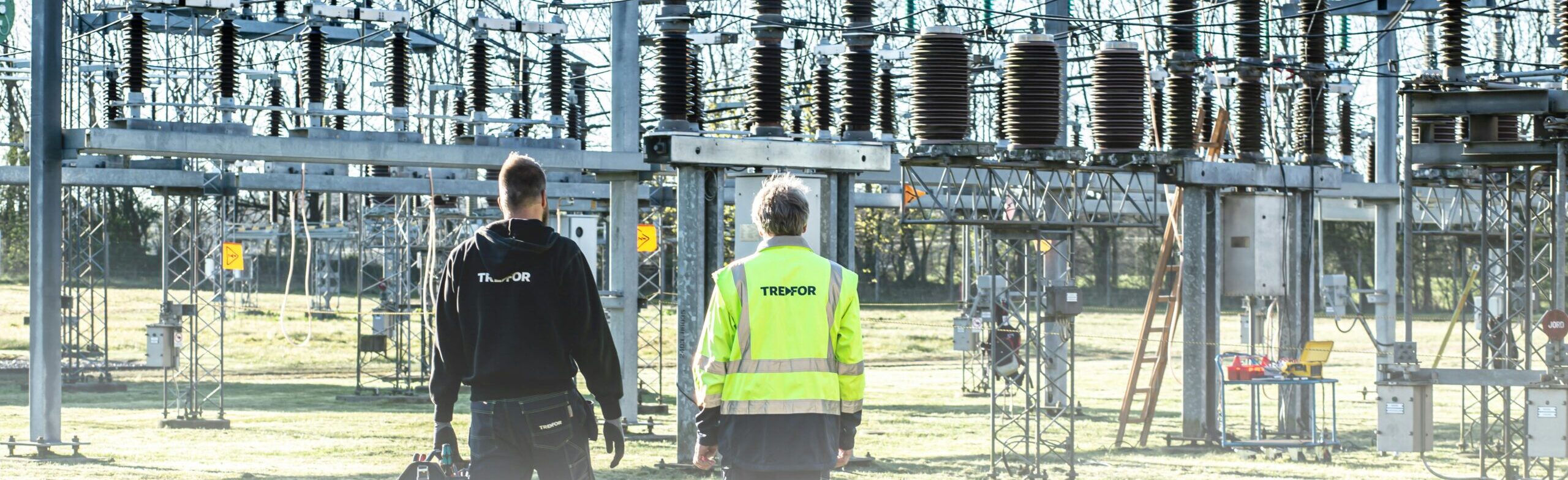 Two workers inspect an outdoor electrical substation, emphasizing safety and maintenance.